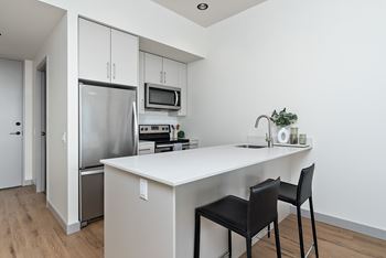A kitchen with a white countertop and black chairs.at Raymond Block, Edmonton Alberta T6E 3R7
